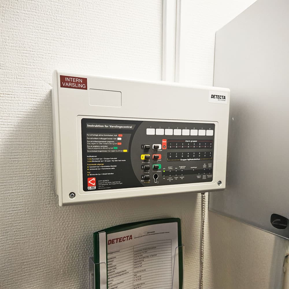 Professionelt nærbillede af en varslingstavle tilknyttet ABA-system, opsat i en teknisk installation hos Detecta. Billedet viser både selve panelet og den tilhørende dokumentation, som hænger lige nedenunder.